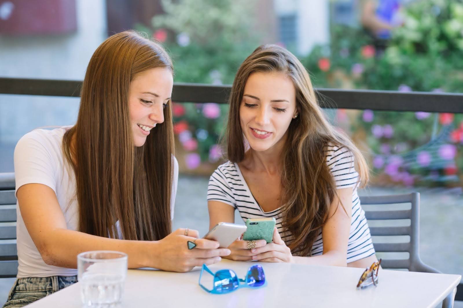 duas mulheres olhando para o celular usando o programa de indicação da UPBET para ganhar dinheiro.