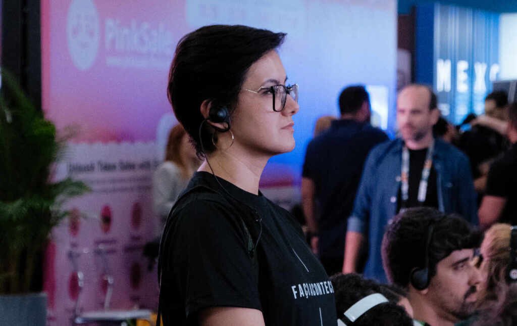 Rika Durão, CEO da Sete Dígitos, nos bastidores de evento corporativo em São Paulo, observando a produção com headset e bolsa tática